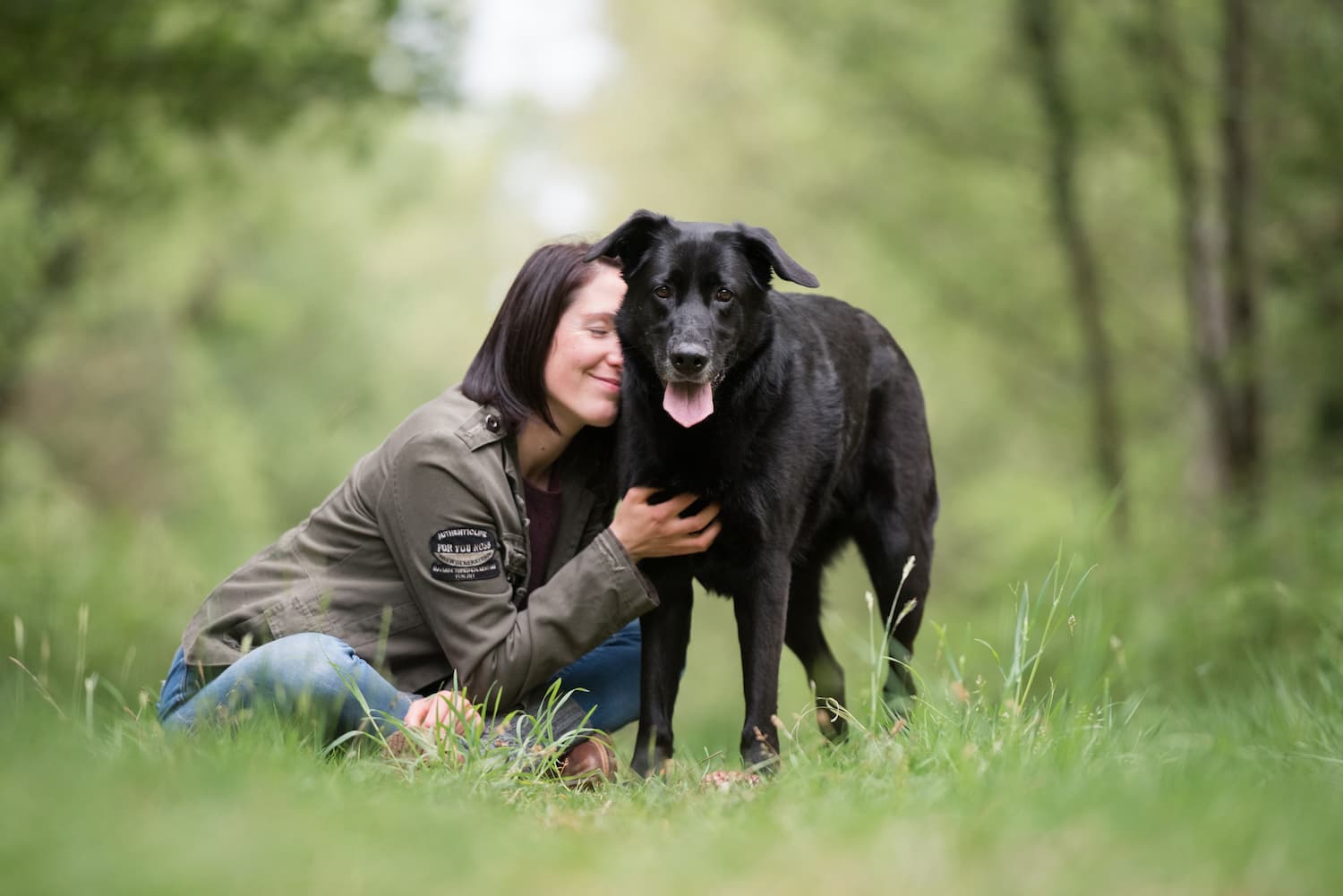 Céline assise dans l'herbe à côté de Vulcain qui est debout et regarde la caméra, elle se blottit contre lui en souriant avec les yeux fermés